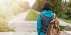 A college student with back turned, wearing a back pack, looking out over college campus, alone