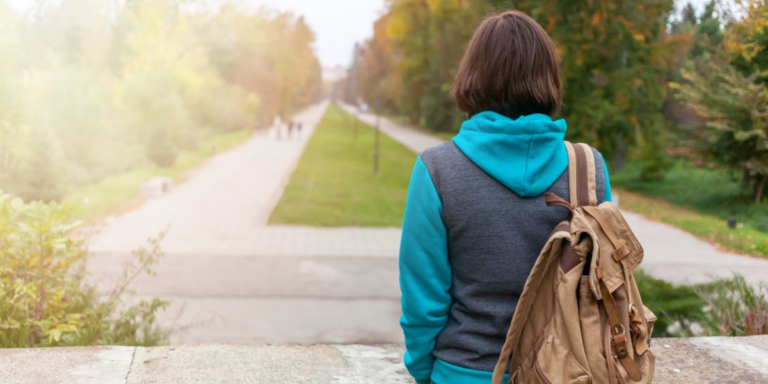 A college student with back turned, wearing a back pack, looking out over college campus, alone