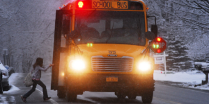 Snowy street in NY. Student boards school bus across the street from house with a for-sale sign