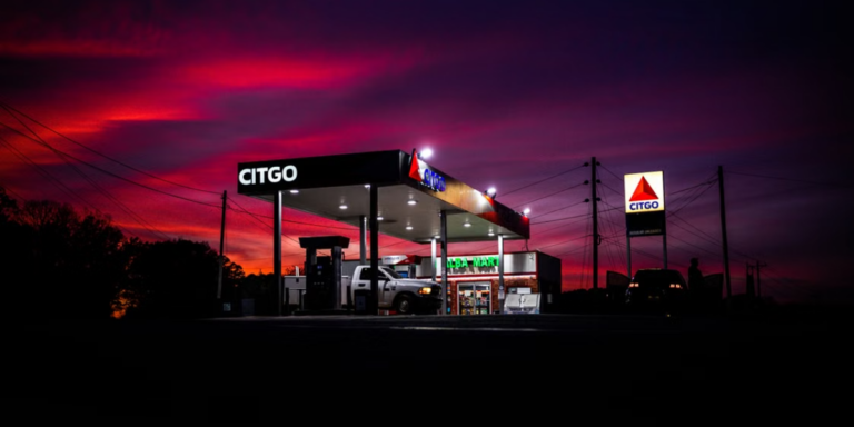 White pick up truck fueling up at a gas station in late evening illuminated by a vivid pink and purple sunset sky